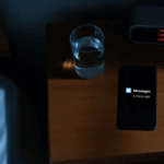 Smartphone glowing with security alert notifications on nightstand at 3 AM with red digital alarm clock showing the time and hand reaching to answer